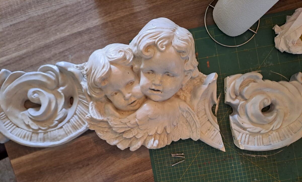 Gebroken engelenornament met losse onderdelen op werkplank